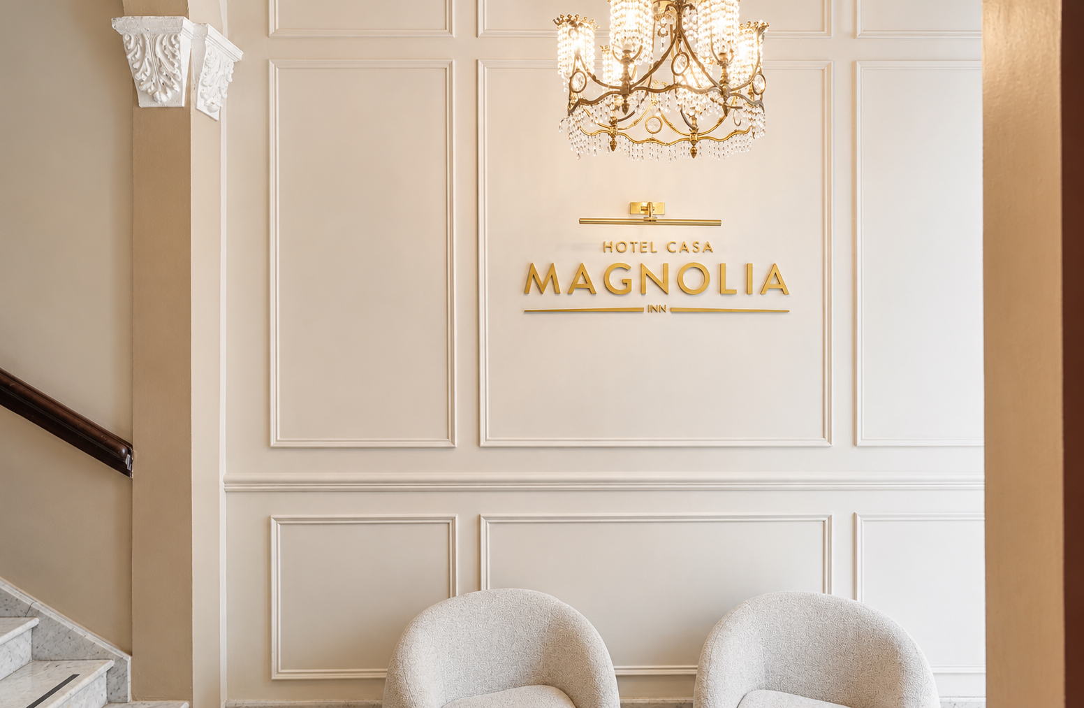 Elegante pared del vest&iacute;bulo con letrero dorado "Magnolia", l&aacute;mpara de ara&ntilde;a y dos sillas blancas.